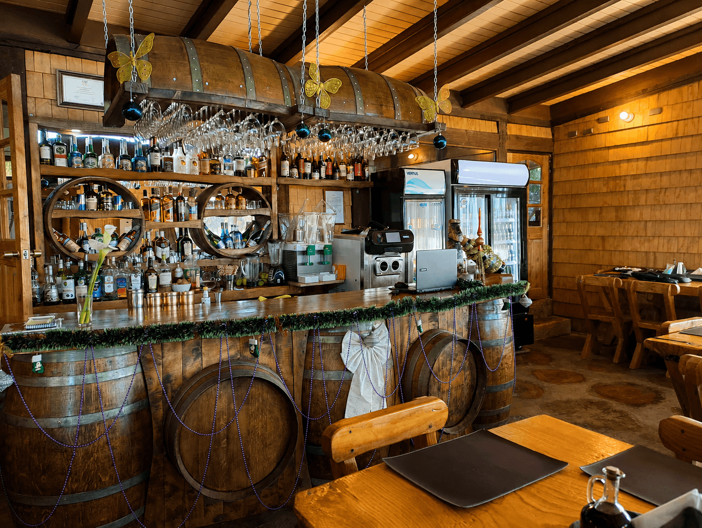 Barra del restaurante montada sobre barricas de vino, con copas colgadas del techo
